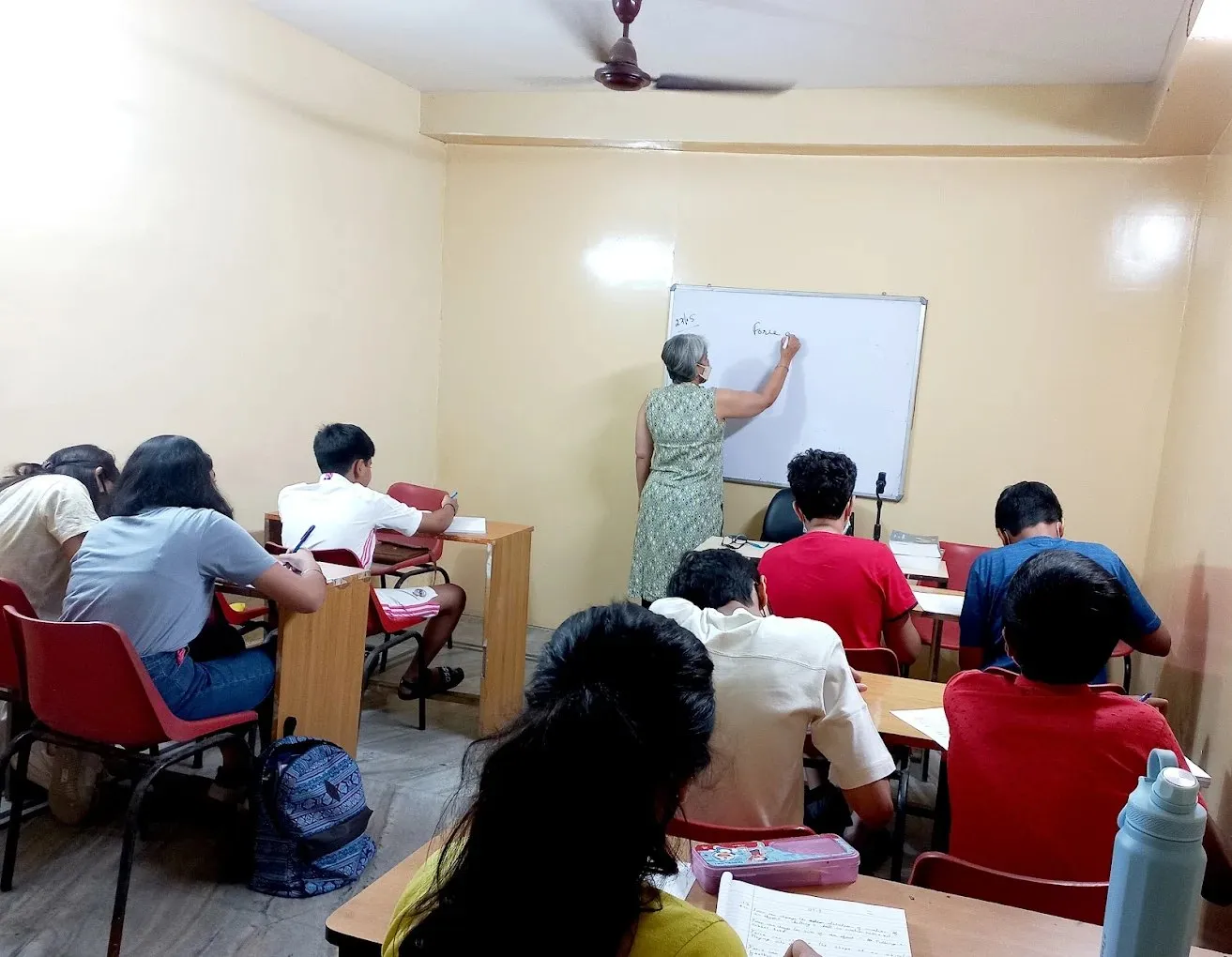 A teacher writing on the whiteboard while the class follows from their desks.