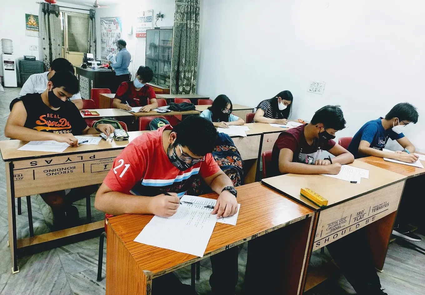 A classroom of students working quietly, the whiteboard behind them.