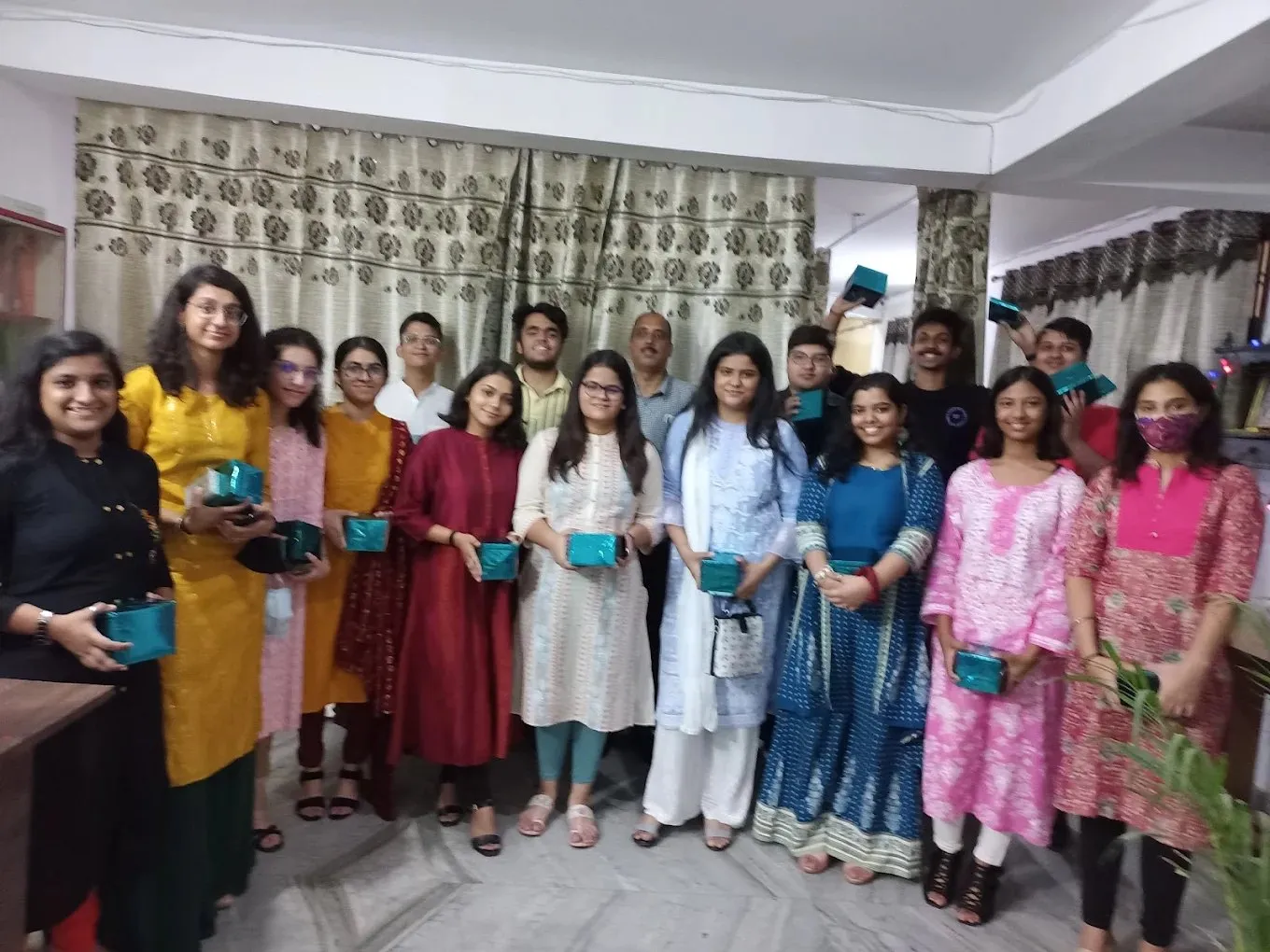 Students and teachers in festive clothes, each holding a small gift box.