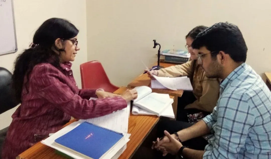 A teacher at a desk with two students, going through their work.