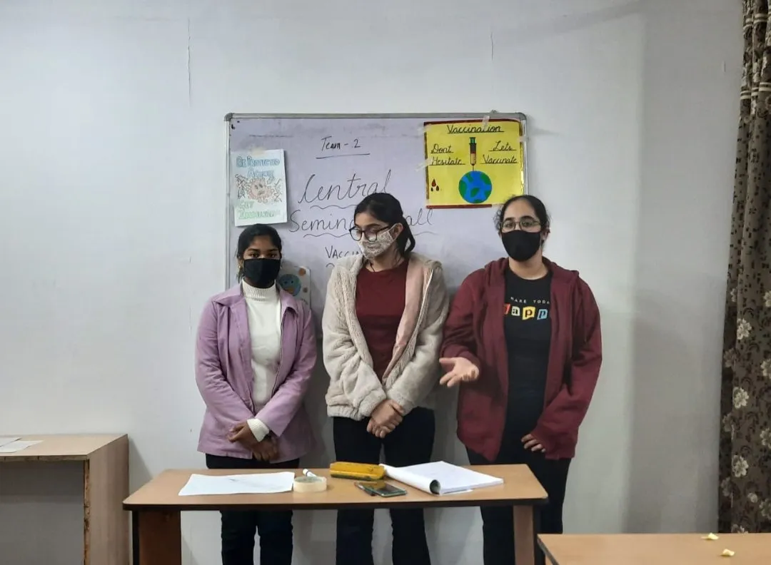 Three students in front of the whiteboard with the posters they made.