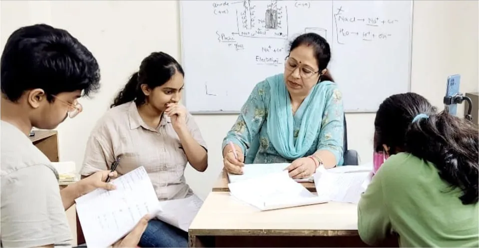 A teacher working through a problem with a group of students around a table.